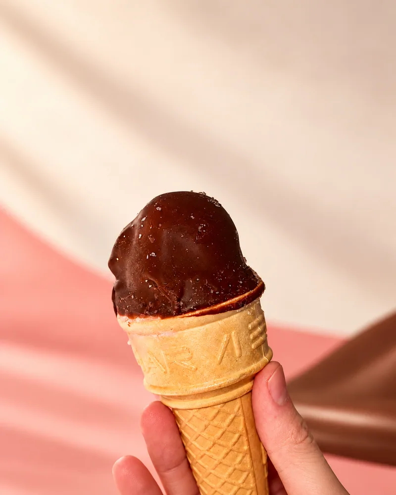 Cone Gelatto com cobertura de chocolate em uma composição de estúdio clara e acolhedora.